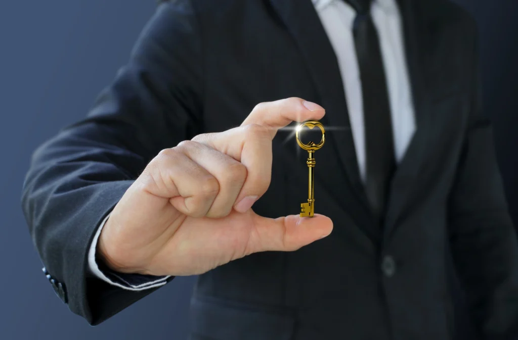 Ein Mann im Anzug hält einen goldenen Schlüssel in der Hand, der auf den Betrachter gerichtet ist. Der Fokus liegt auf dem Schlüssel, während der Mann und der Hintergrund unscharf sind, was symbolisch für die Schlüsselrolle eines Arbeitsvertrages stehen könnte.